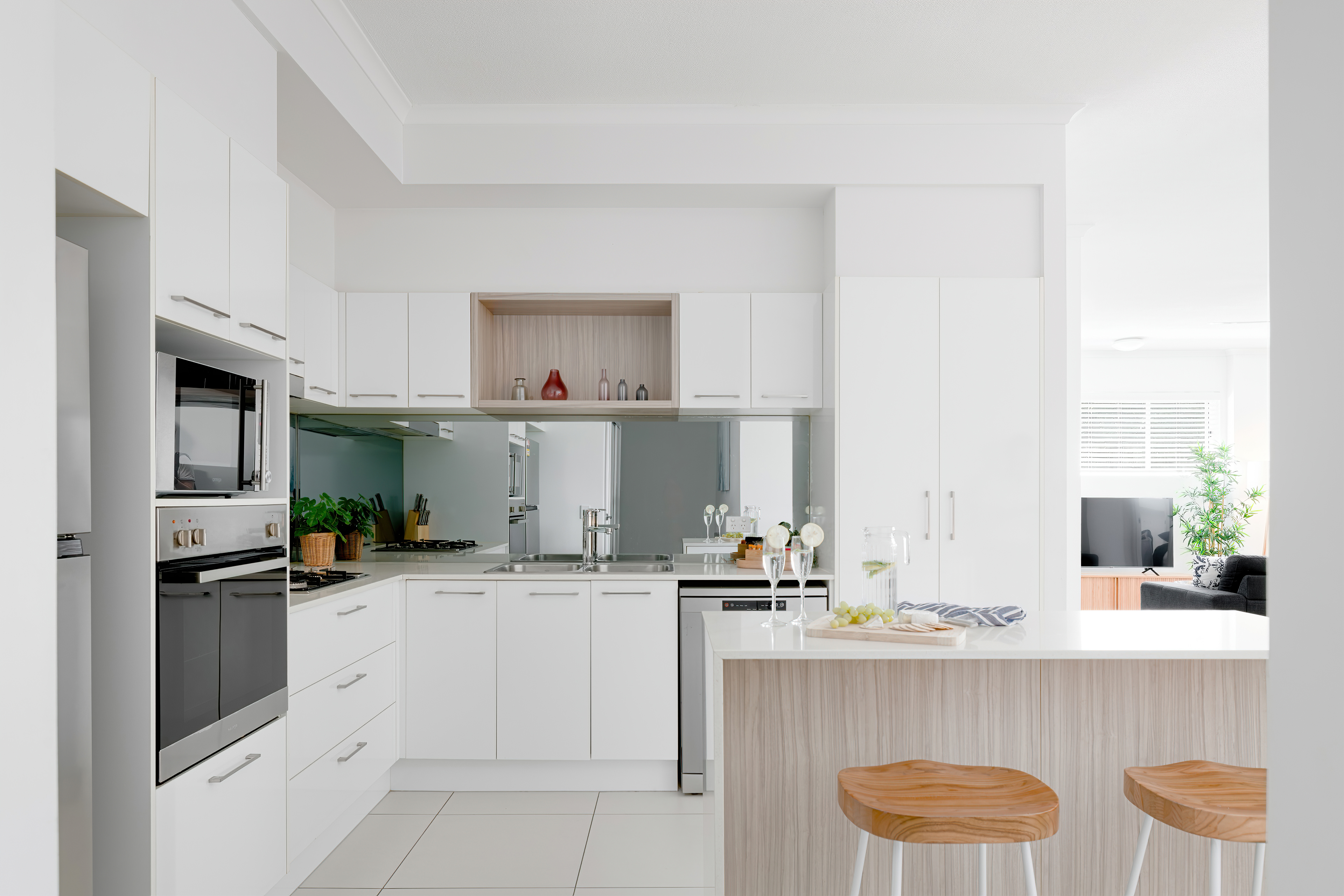 Bright white kitchen with island bench and bar stools opening to the living area