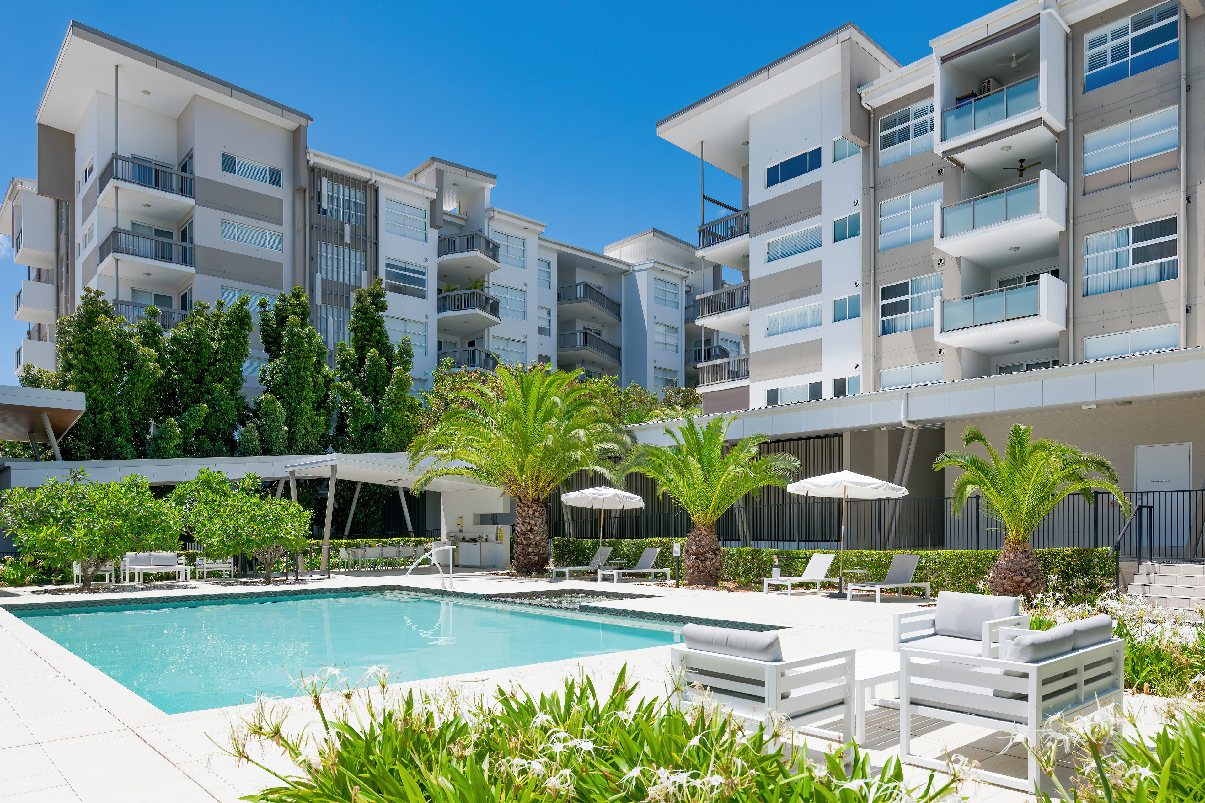Resort-style pool and spa with sun loungers, palms and the apartment building behind